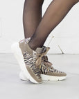 Zebra-patterned sneakers worn with sheer black tights on a light background