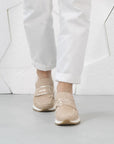 Beige sneakers worn with white pants on a light gray floor.